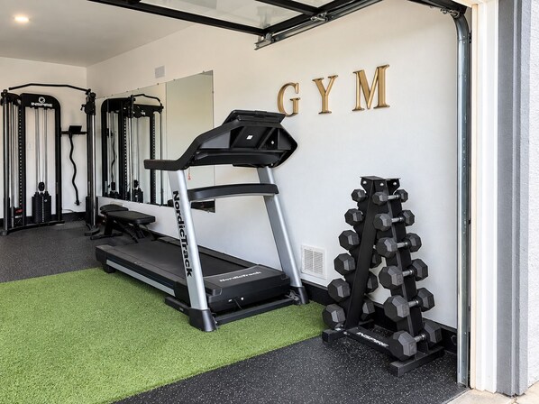 Un gimnasio con cinta de correr, banco de pesas y mancuernas.