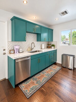 Una cocina moderna con gabinetes color turquesa, un lavavajillas de acero inoxidable y un refrigerador compacto.