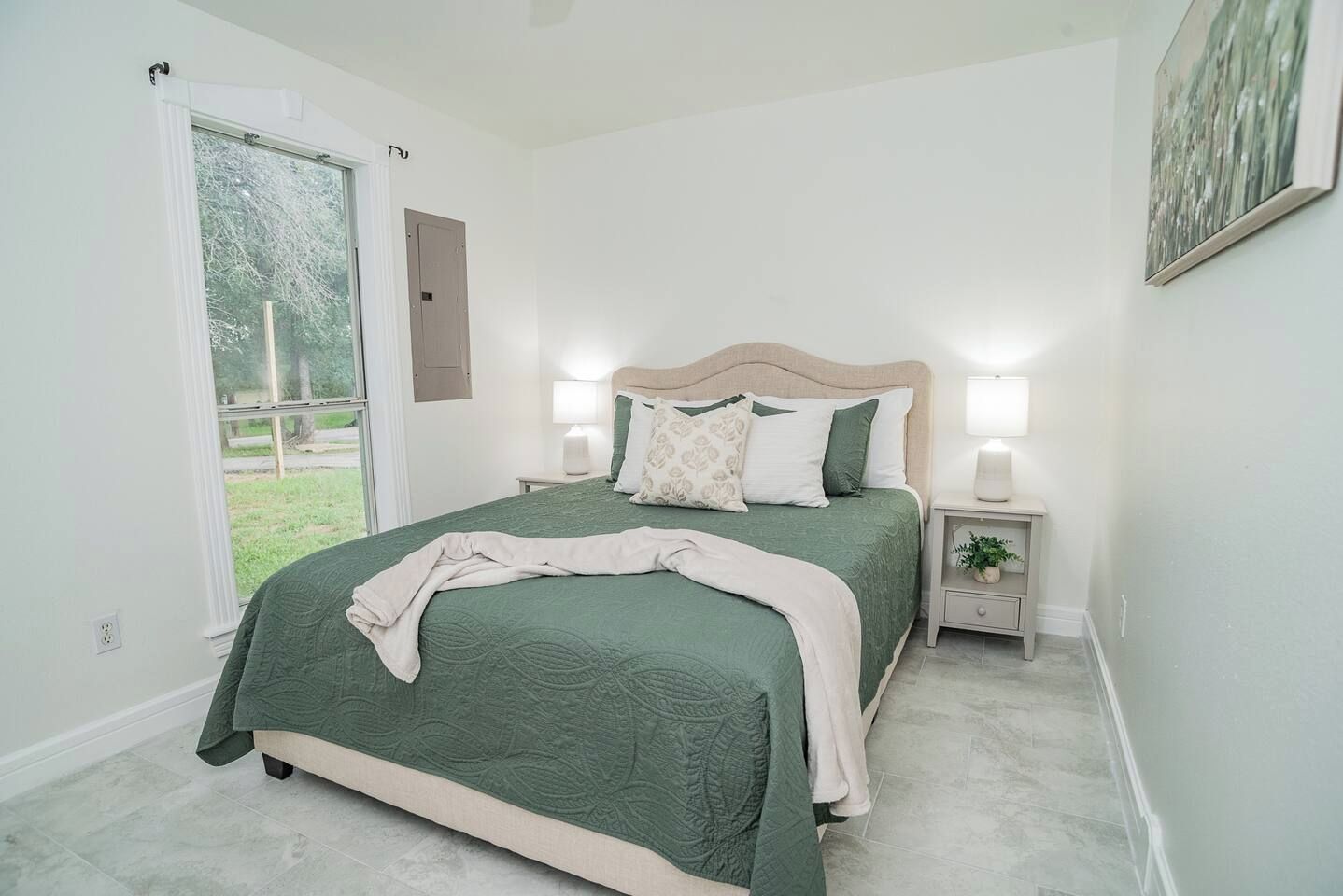 Un dormitorio con cama, mesitas de noche, una ventana y una puerta.