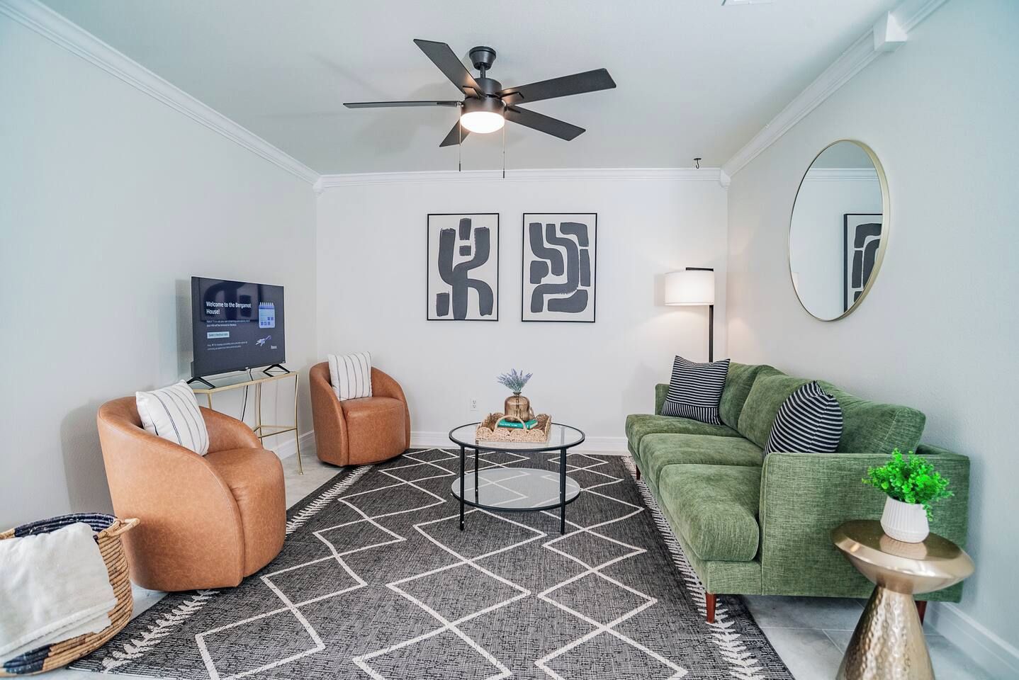Un salon comprenant un canapé, deux fauteuils, une table basse, un téléviseur, un ventilateur de plafond et un miroir.