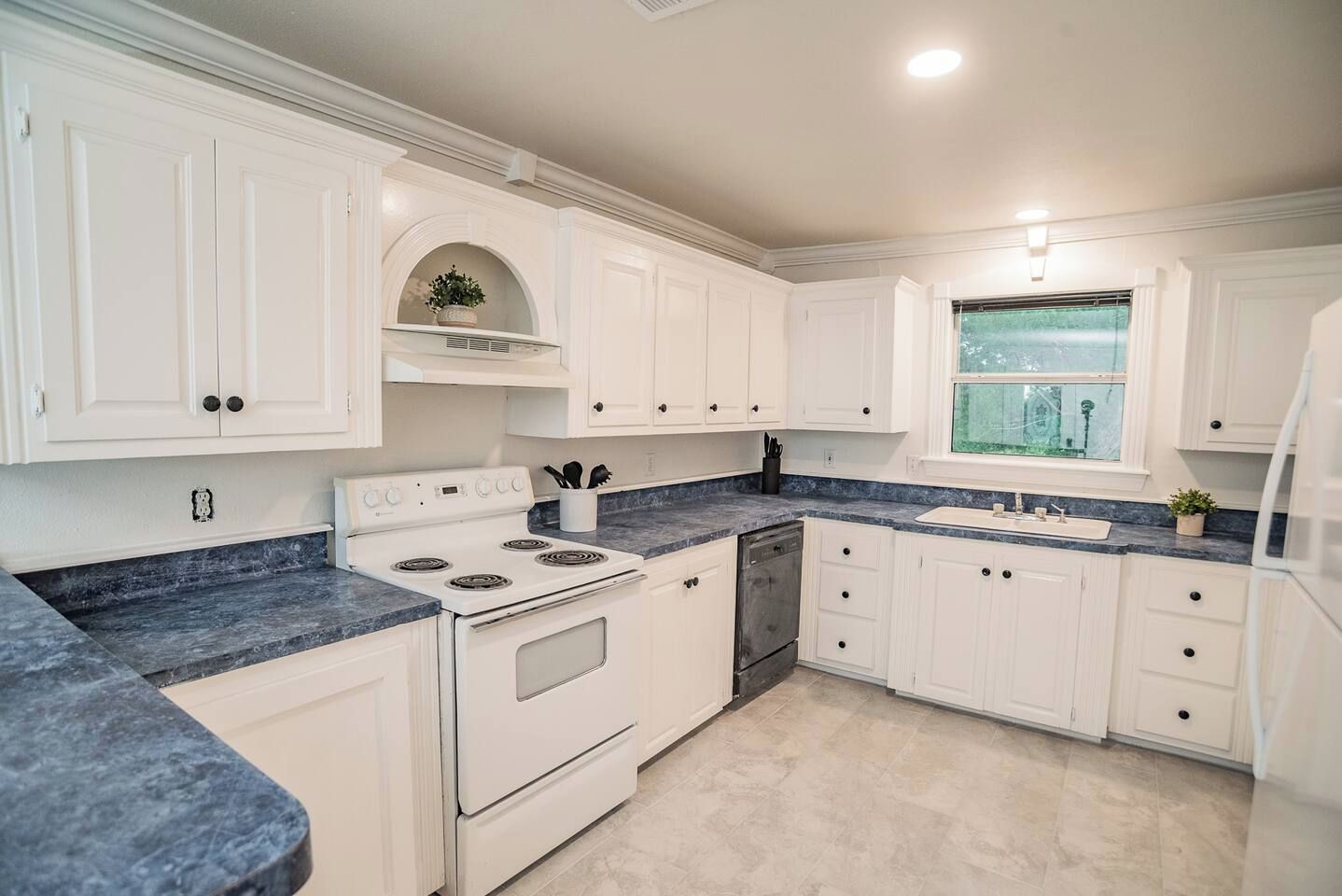 A kitchen with white cabinetry, a stove, a dishwasher, and a window with a view.