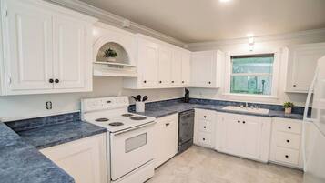 A kitchen with white cabinetry, a stove, a dishwasher, and a window with a view.