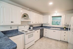 A kitchen with white cabinetry, a stove, a dishwasher, and a window with a view. - Bergamot House-Luling Texas (Luling)