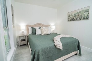 A bedroom with a bed, nightstands, a bedside lamp, a window, and a wall-mounted painting. - Bergamot House-Luling Texas (Luling)