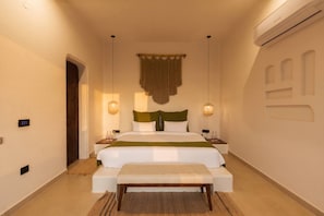 Een slaapkamer met een bed, nachtkastjes, een bankje, een wandairconditioner en een deur.