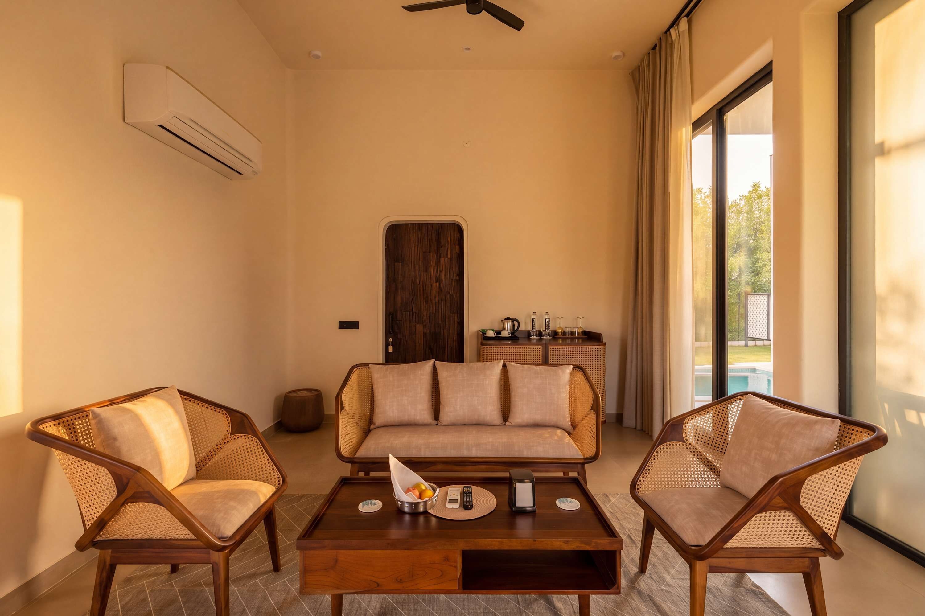 A room with a sofa, two armchairs, a coffee table, and a view of a pool.