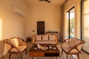 Een kamer met een bank, twee fauteuils, een bijzettafeltje en uitzicht op een zwembad.