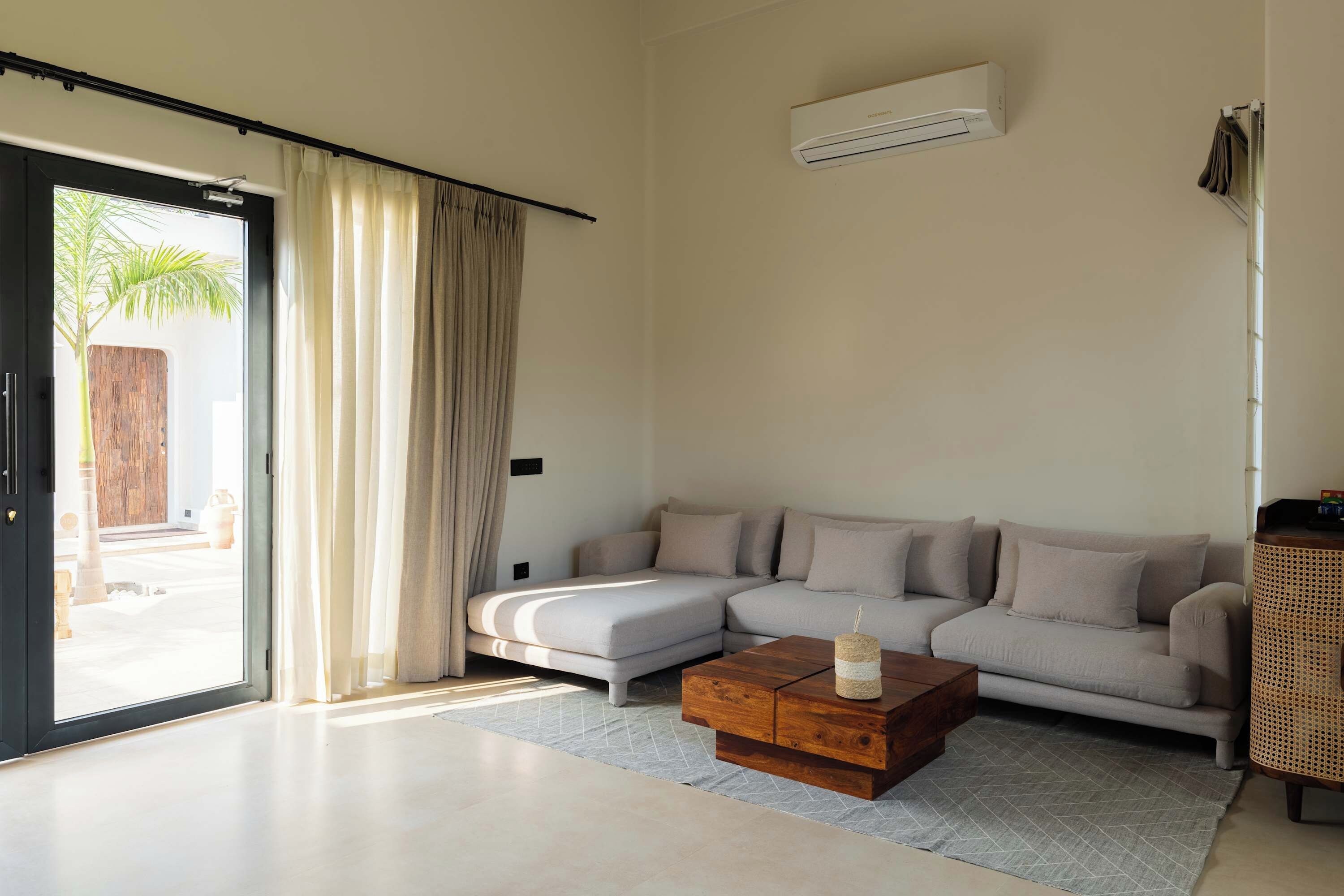 Una sala de estar moderna con un sofá seccional, una mesa de centro de madera y un amplio ventanal corredero que da a un espacio exterior.