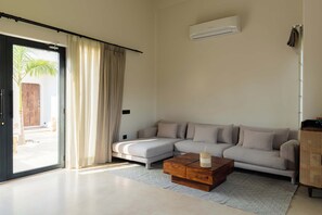 Een moderne woonkamer met een modulaire bank, een houten salontafel en een grote schuifglazen deur die leidt naar een buitenruimte.
