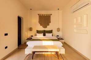 Ein modernes Schlafzimmer mit Bett, Nachttischen, einer Bank, einer wandmontierten Klimaanlage und einem Wandbild.
