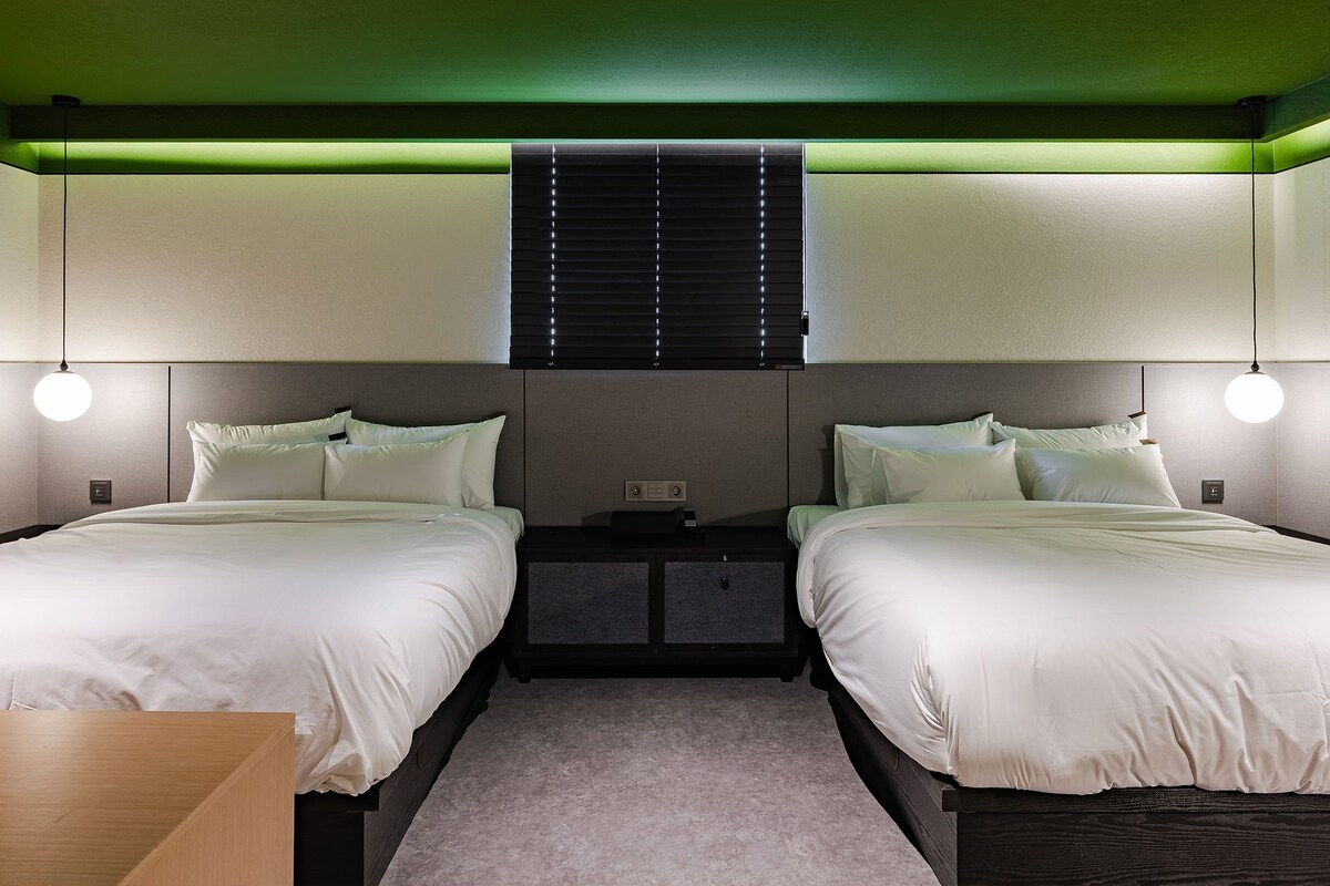 Habitación de hotel con dos camas, una mesita de noche y techo verde.