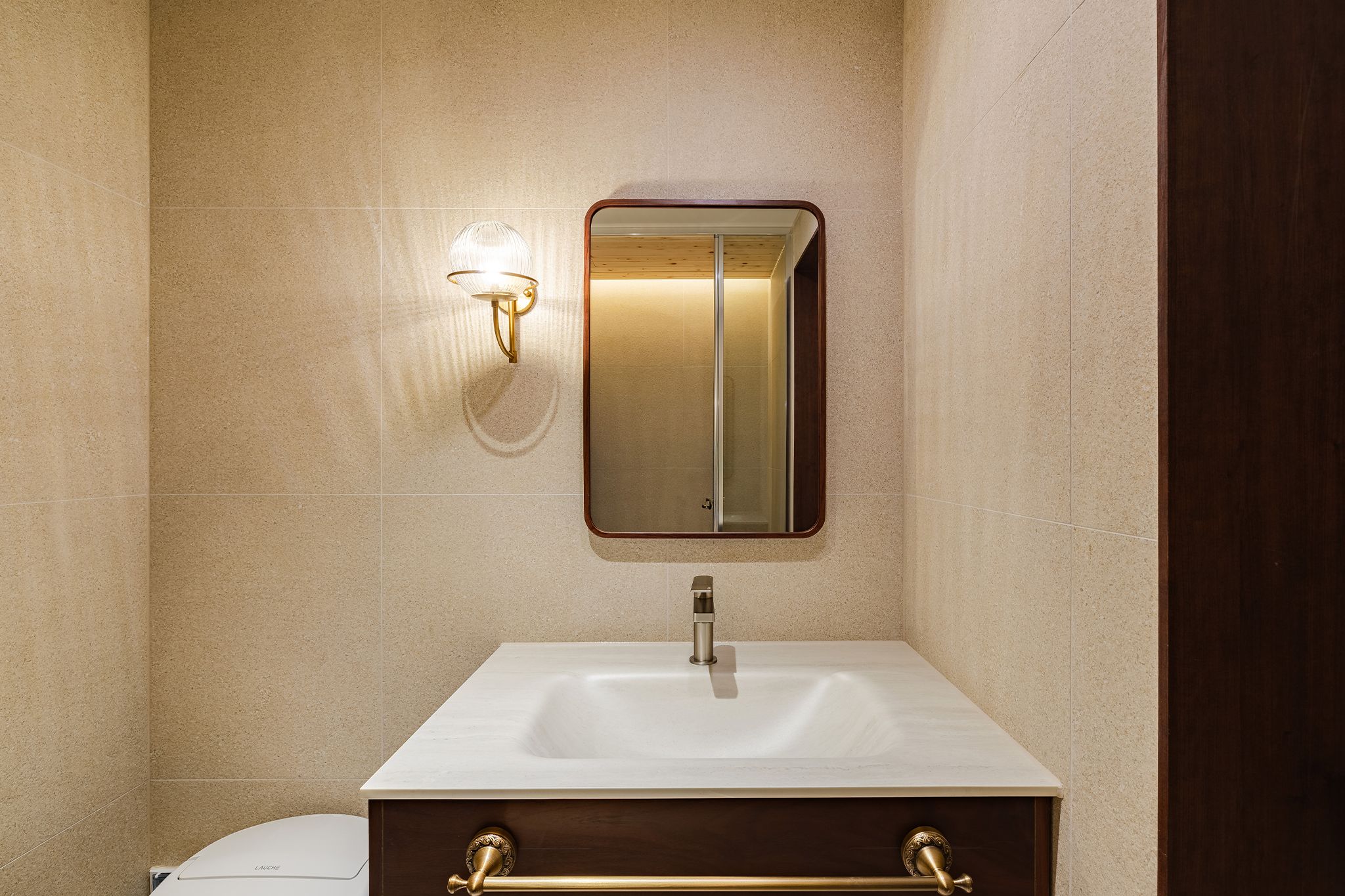 A bathroom with a white sink, a mirror, and a wall-mounted light fixture.