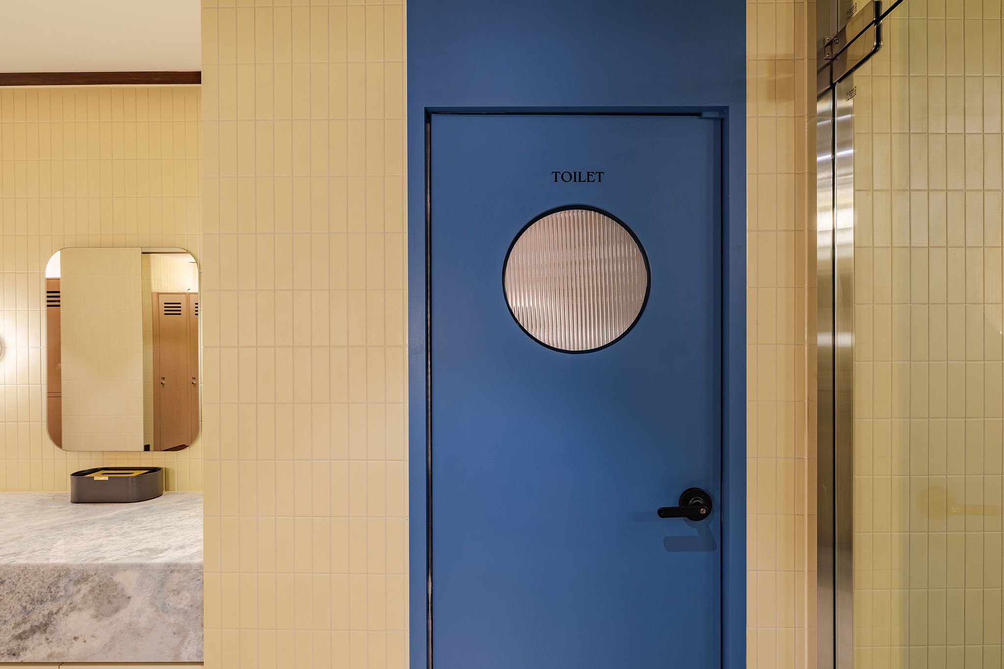 Una puerta azul con un ventanal circular y la palabra 'TOILET' escrita encima.