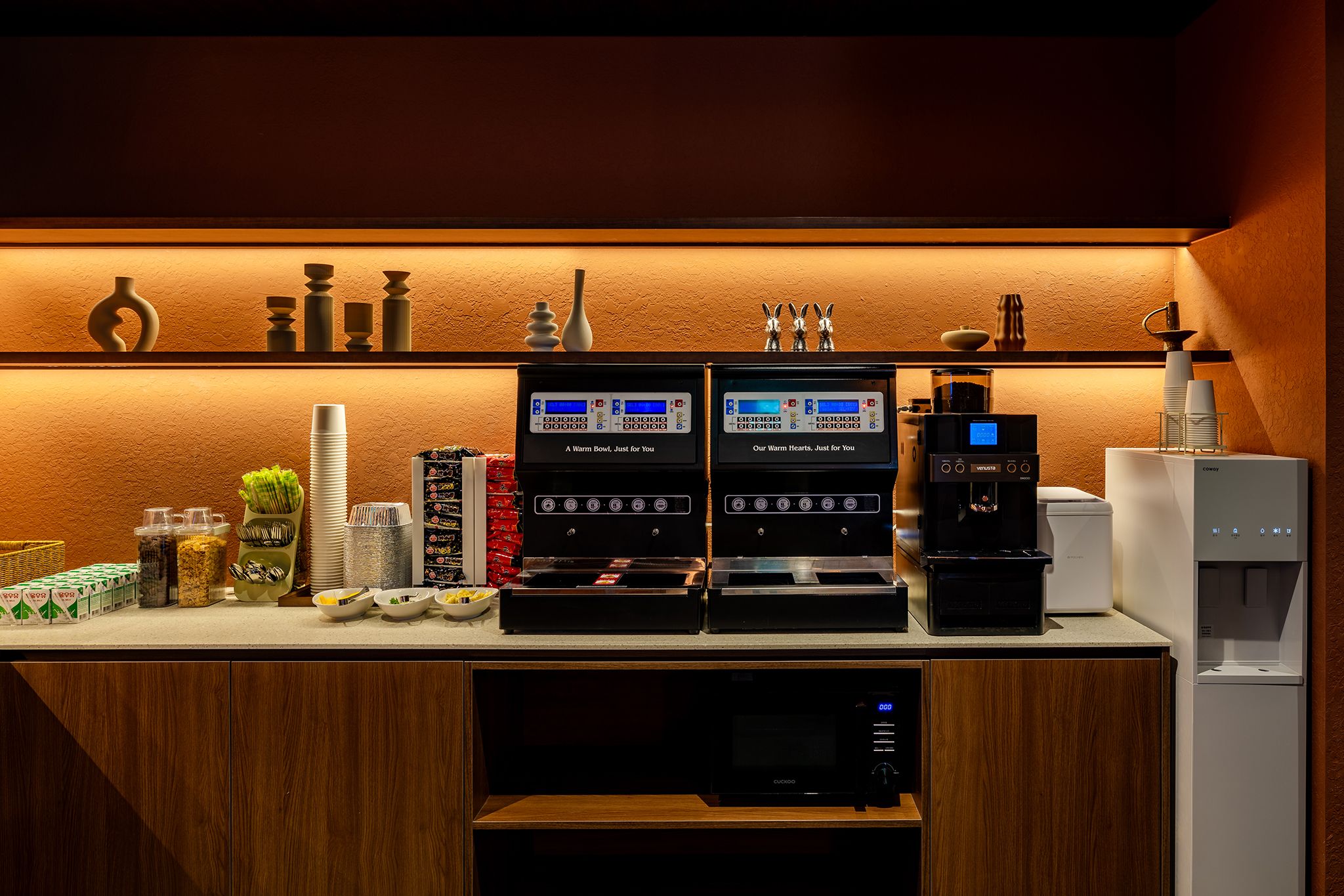 A coffee station with two coffee machines, a water dispenser, and various coffee cups and saucers.