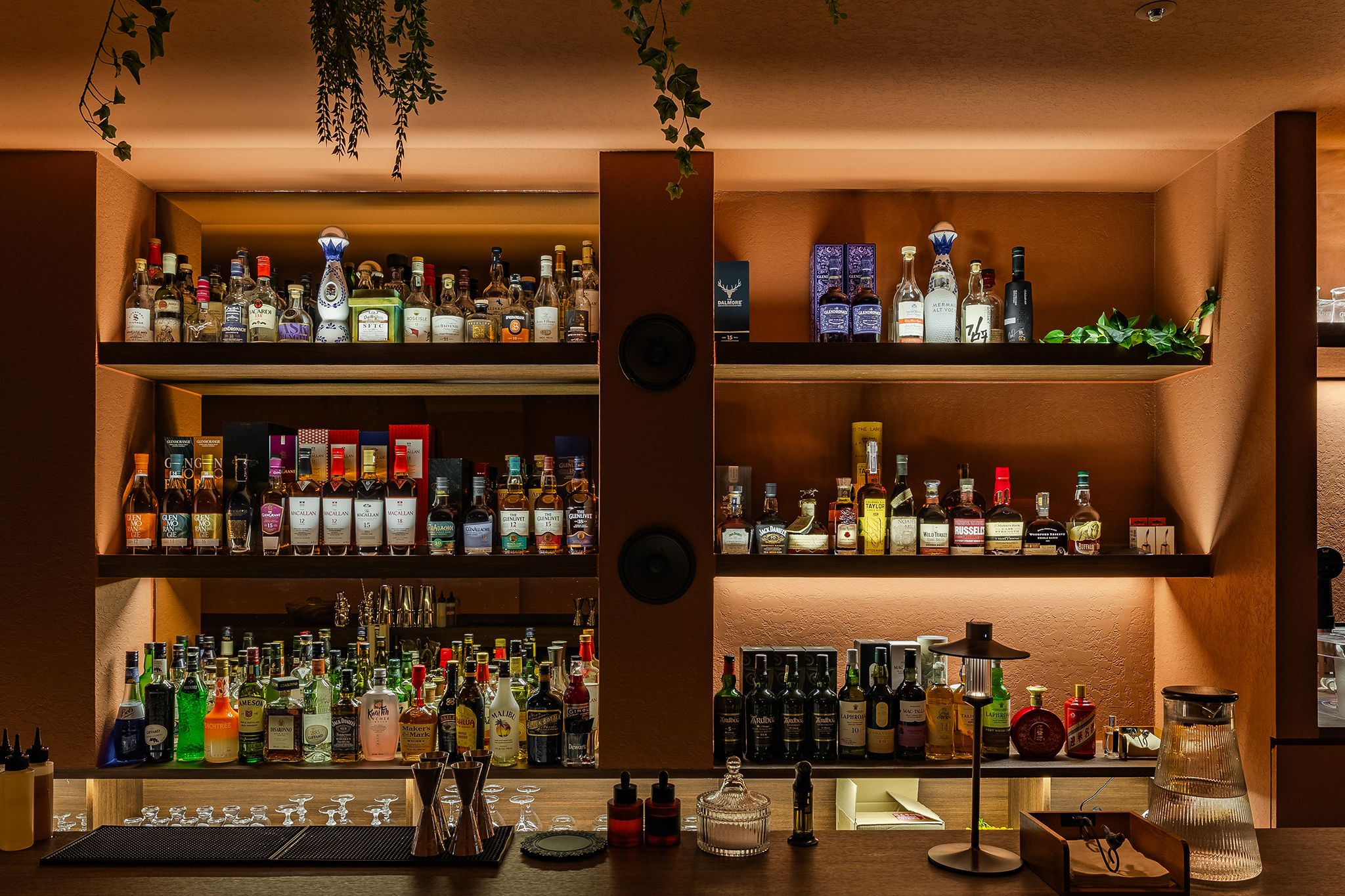 Bar com várias prateleiras repletas de garrafas de bebidas e copos.