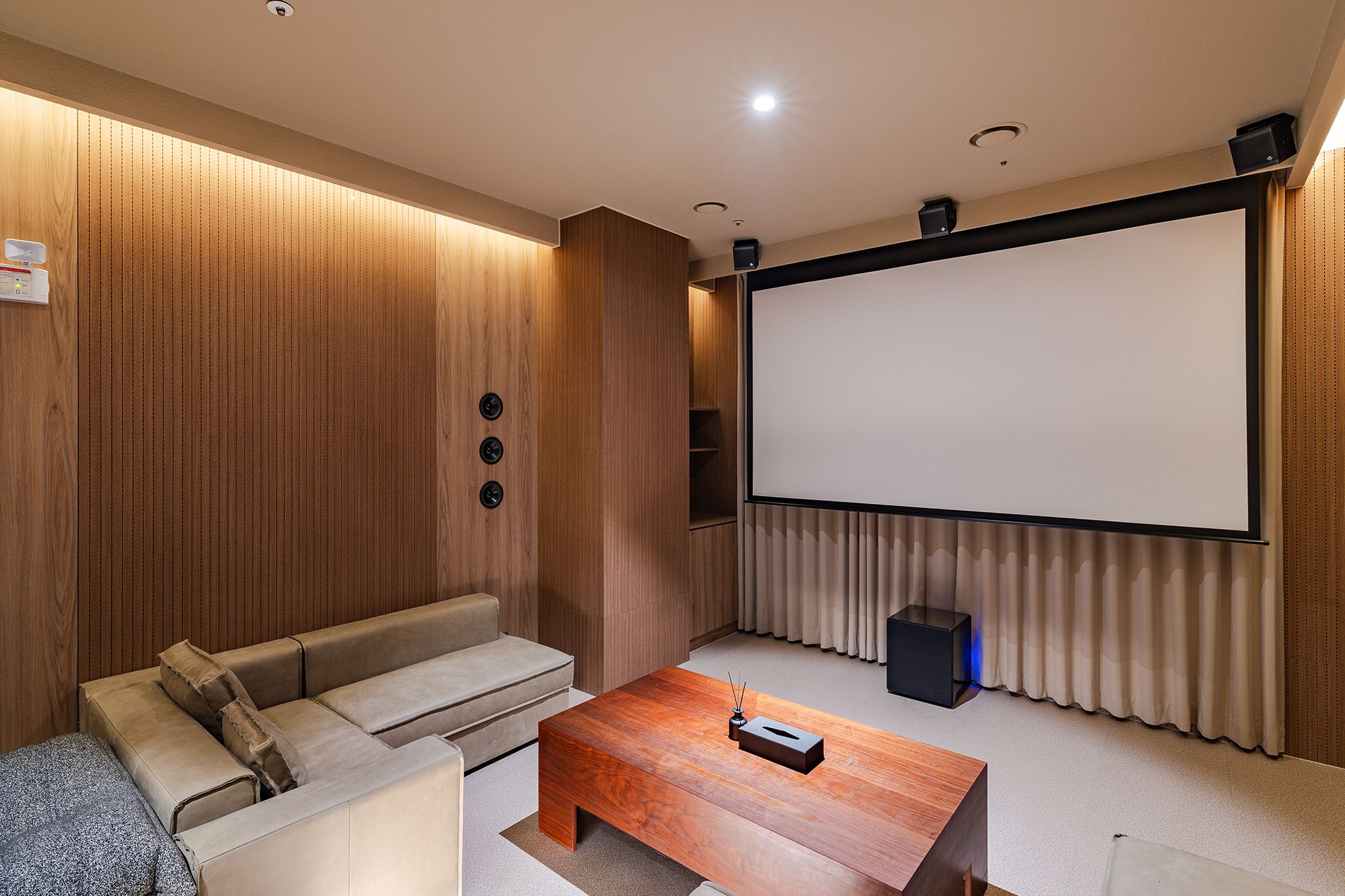 A home theater room with a large screen, a sofa, a coffee table, and a speaker.