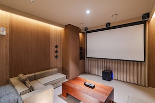 Una sala de cine en casa con una pantalla grande, un sofá, una mesa de centro y un altavoz.