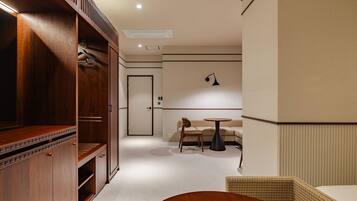A hotel room with a wooden wardrobe, a round table, a sofa, and a wall-mounted lamp.