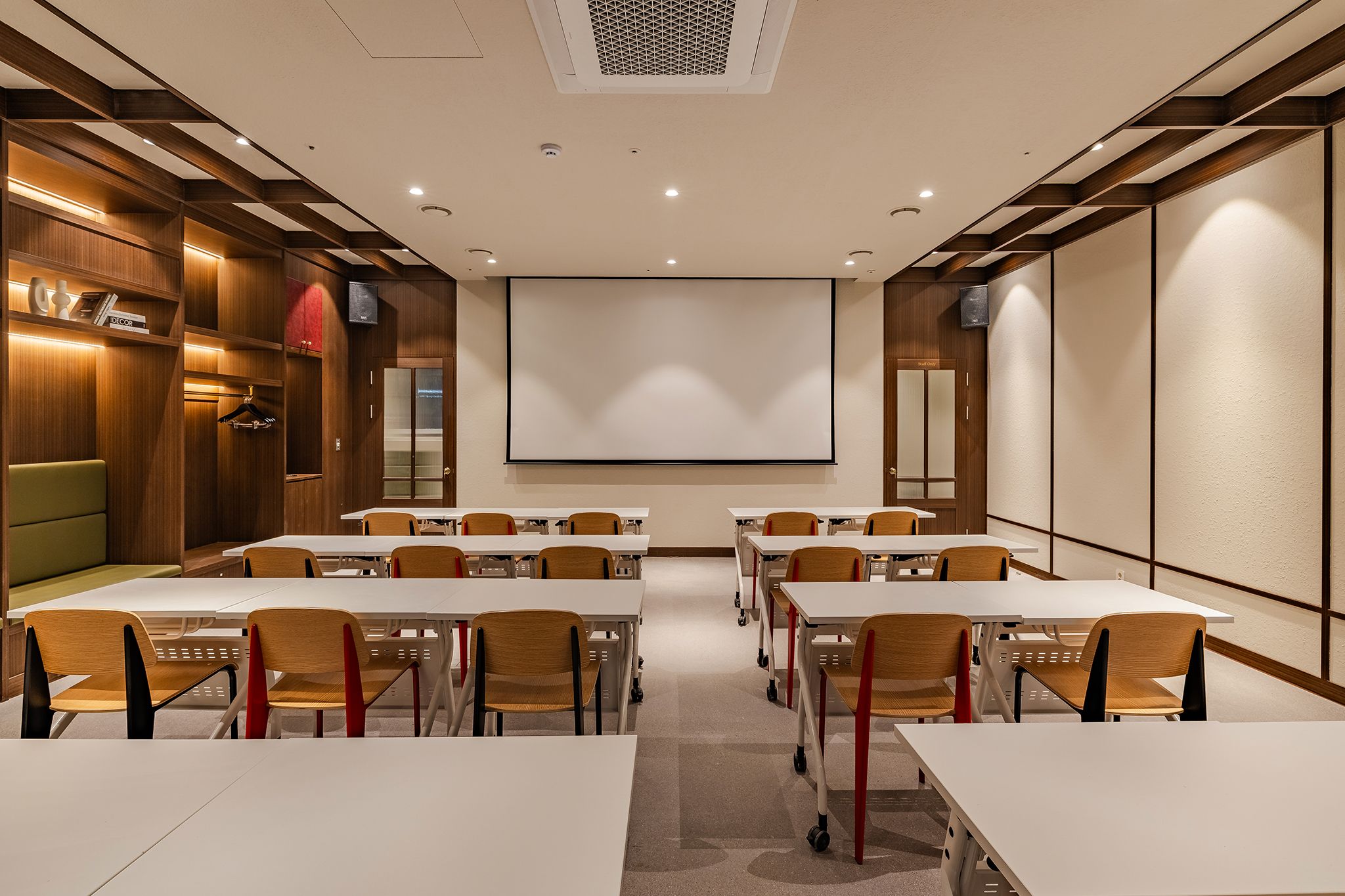 A conference room with white tables, wooden chairs, a projector screen, and a large whiteboard.