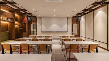 A conference room with white tables, wooden chairs, a projector screen, and a large whiteboard.