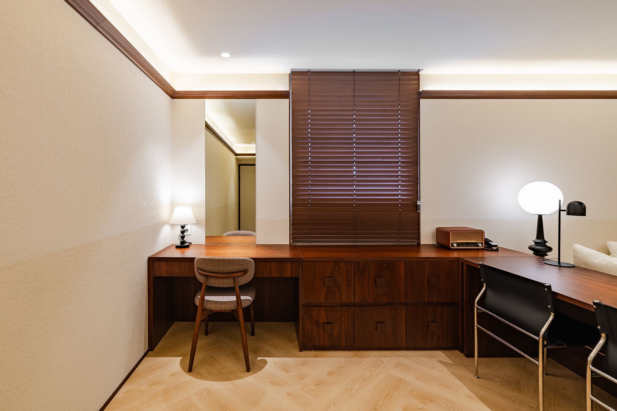 A compact office space with a wooden desk, two chairs, a lamp, and a window with blinds.