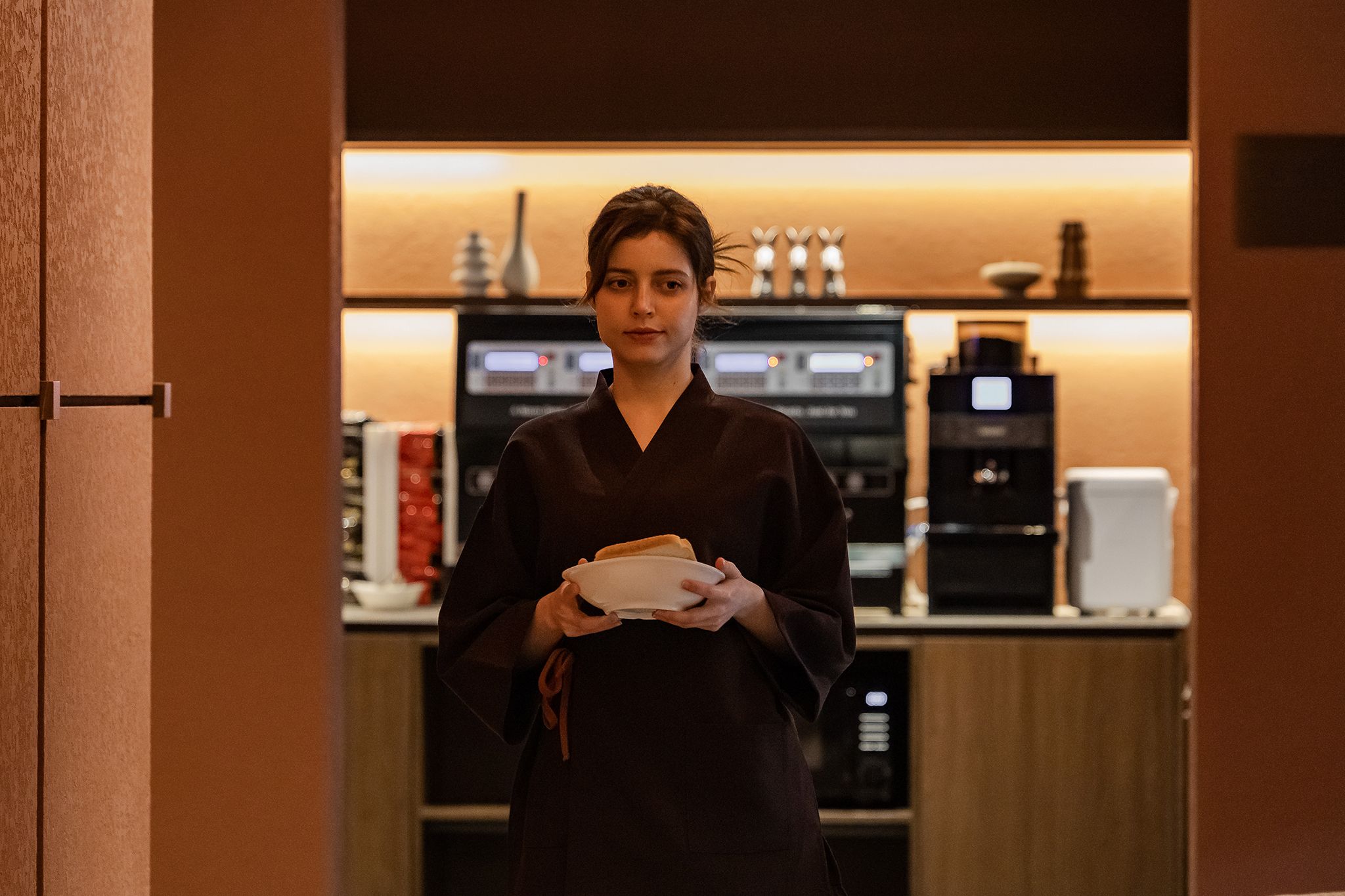 A person holding a plate in a room with a coffee machine and a microwave in the background.