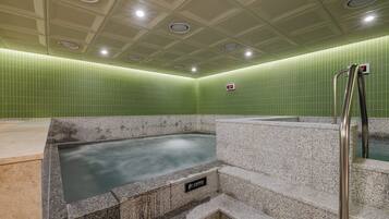 A hot tub area with a caution sign, tiled walls, and a metal handrail.
