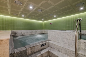 A hot tub area with a caution sign, tiled walls, and a metal handrail. - Mansion Bridge Cheonan (Cheonan)