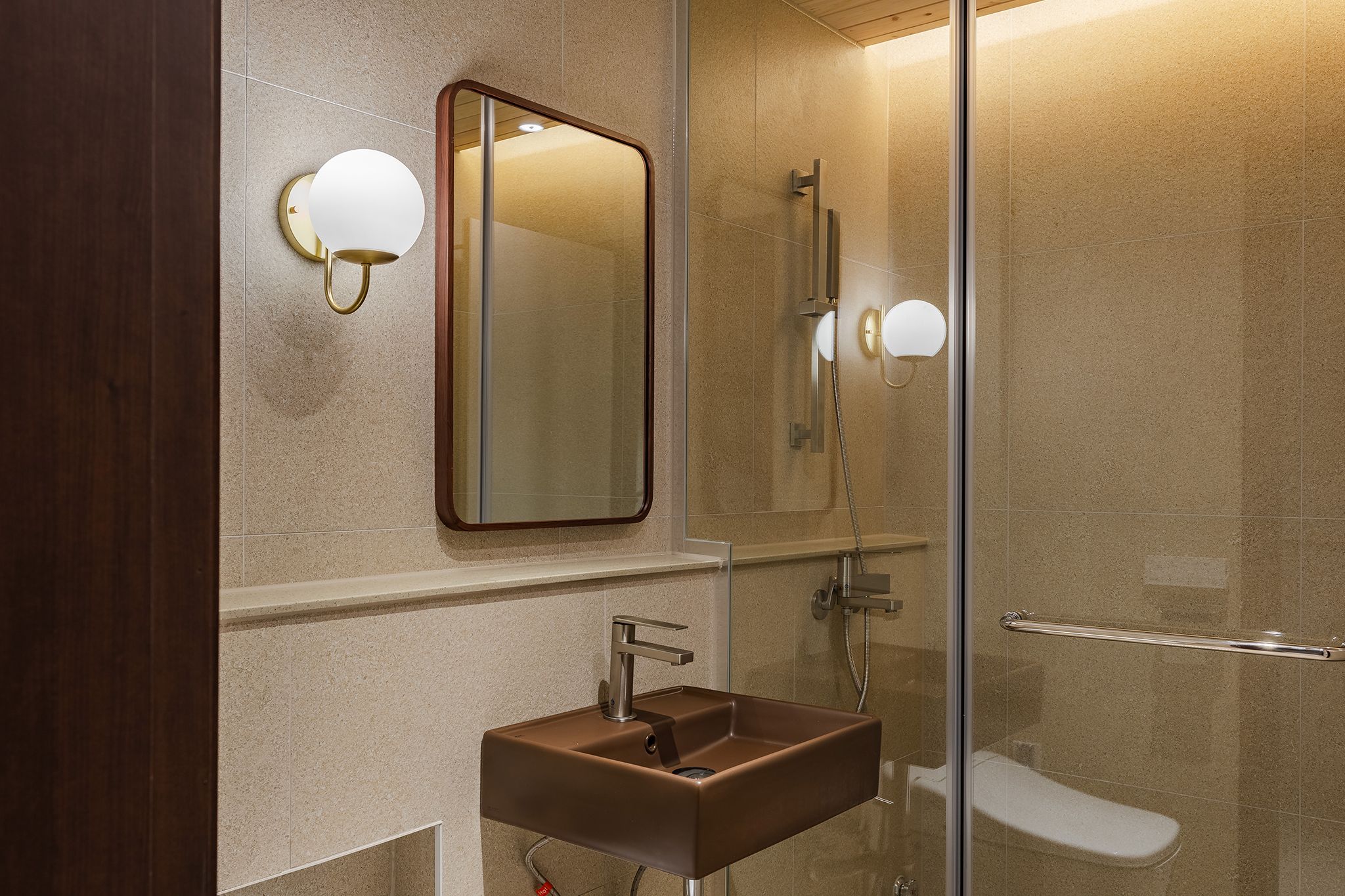 Un baño moderno con ducha envuelta en vidrio, lavamanos de madera e iluminación empotrada.