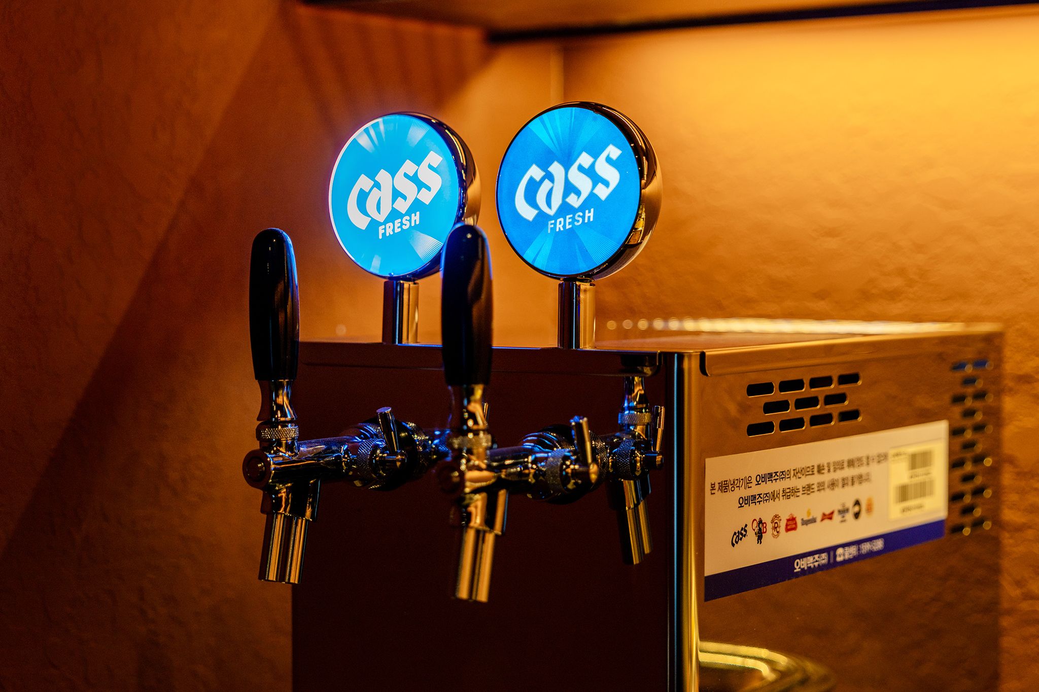 A tap with two blue labels reading 'Cass Fresh' and a metal box with text and logos.