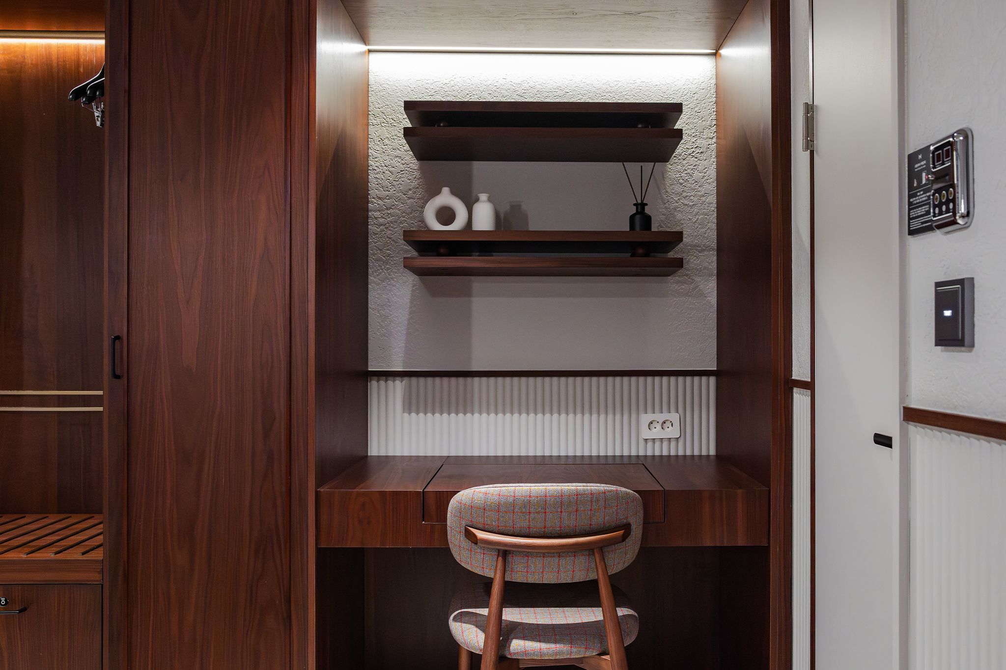 A compact, modern office space with a wooden desk, a chair, and built-in shelves above.
