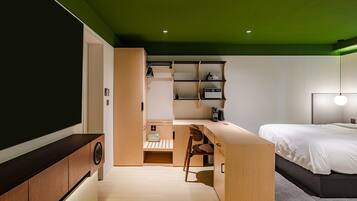 A modern bedroom with a bed, a desk, and a chair. There is a shelf unit with various items on it.