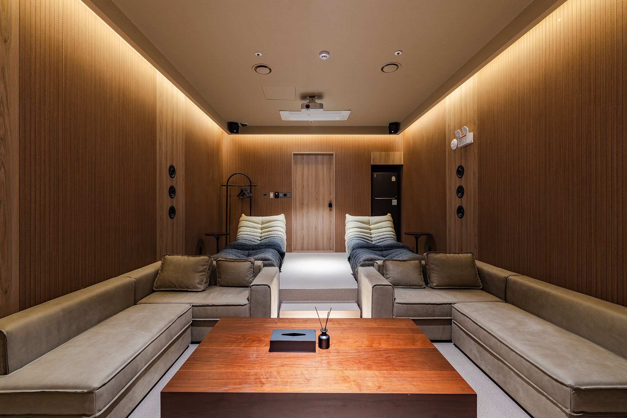 Una habitación moderna y bien iluminada, con un panel de madera en la pared, un conjunto de sofás centrales, una mesa de centro y una puerta en la parte posterior.