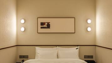 Una habitación de hotel con cama, mesitas de noche, un cuadro enmarco y lámparas fijadas a la pared.