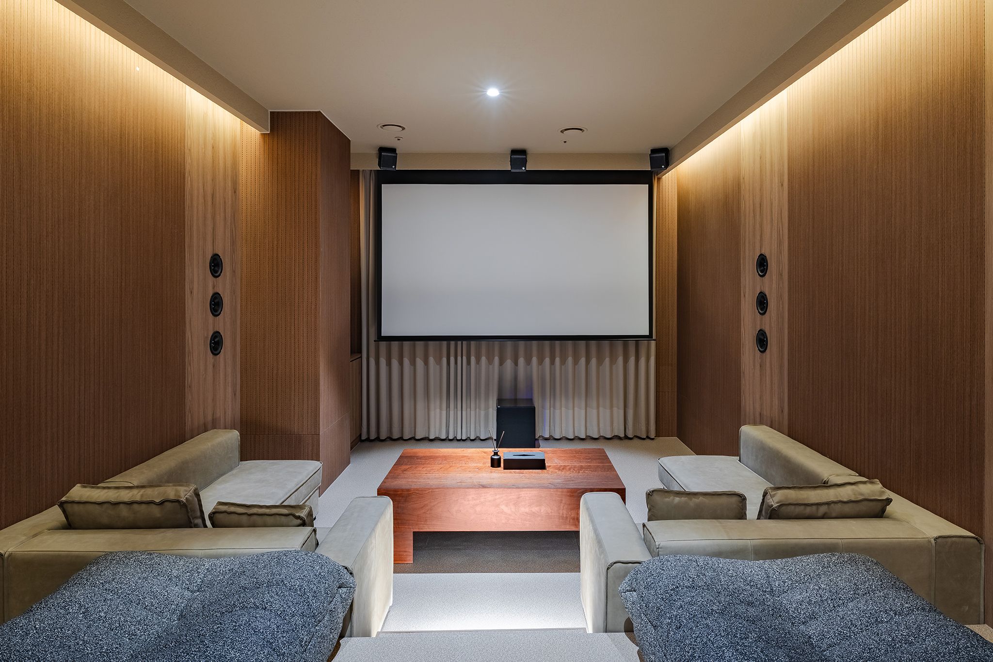 Un cine en casa con una pantalla grande, asientos cómodos y paneles de madera.