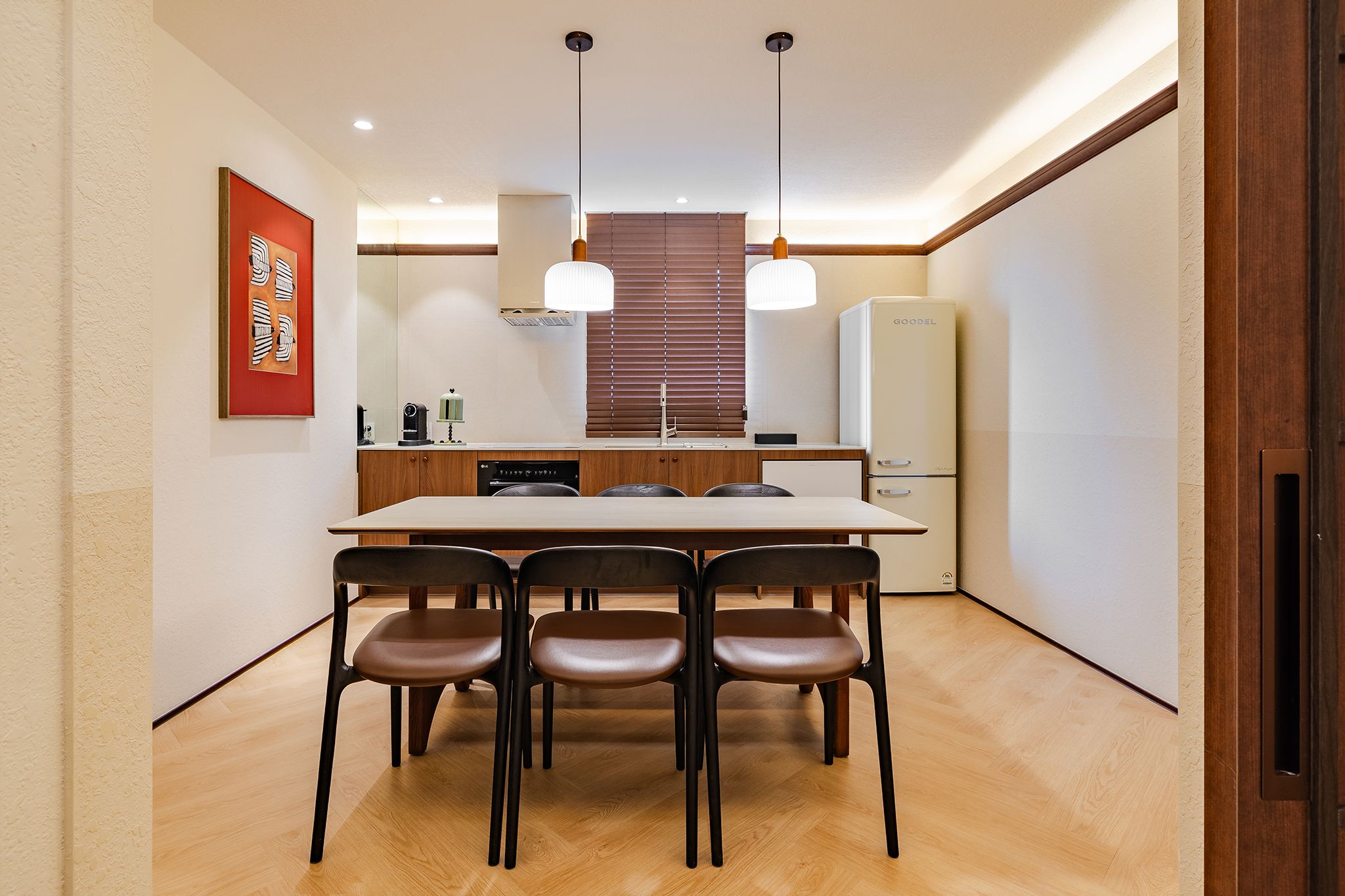 A modern kitchen with a dining table, chairs, pendant lights, and a refrigerator.