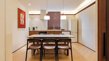 A modern kitchen with a dining table, chairs, pendant lights, and a refrigerator.