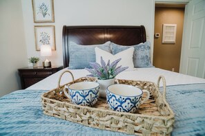 A neatly made bed with a blue and white patterned bedspread, a dark wooden headboard, and a bedside table with a lamp and a small plant. - Red Barn Lake House-Lake McQueeney (Seguin)