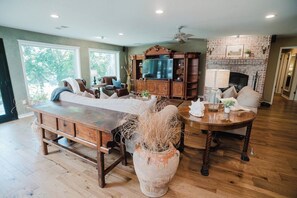 A spacious living room with a large wooden table, a fireplace, and a television. - Red Barn Lake House-Lake McQueeney (Seguin)