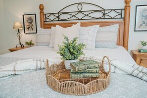 Een net opgemaakt bed met hoofdbord, een nachtkastje met een lamp en een wand met ingekaderde kunstwerken.