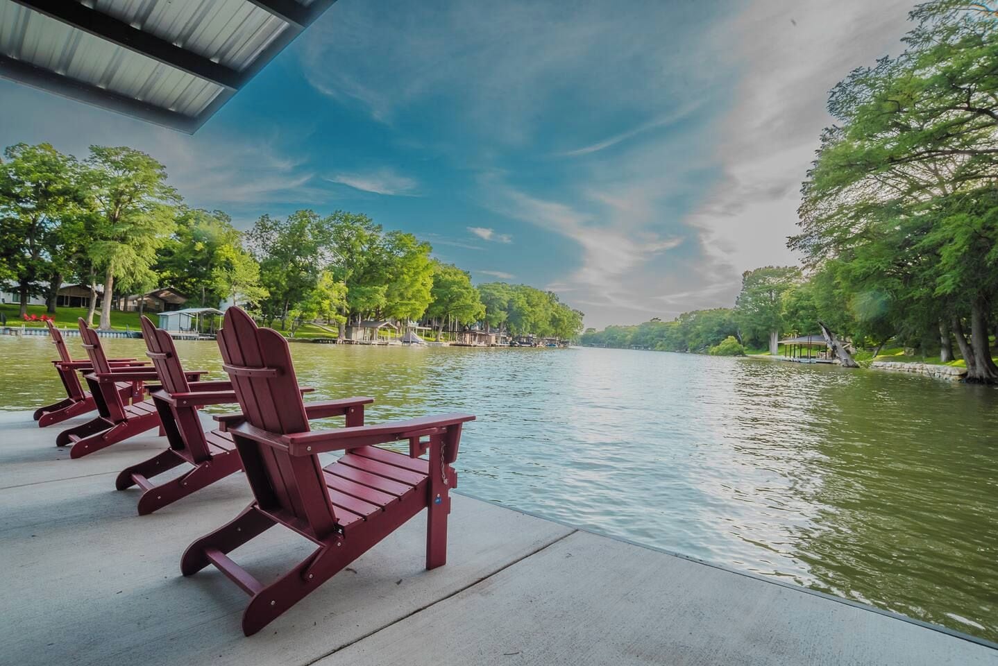 A waterfront view with Adirondack chairs and a dock.