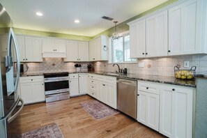 A kitchen with white cabinets, a stainless steel refrigerator, a built-in oven, a dishwasher, and a granite countertop. - Red Barn Lake House-Lake McQueeney (Seguin)