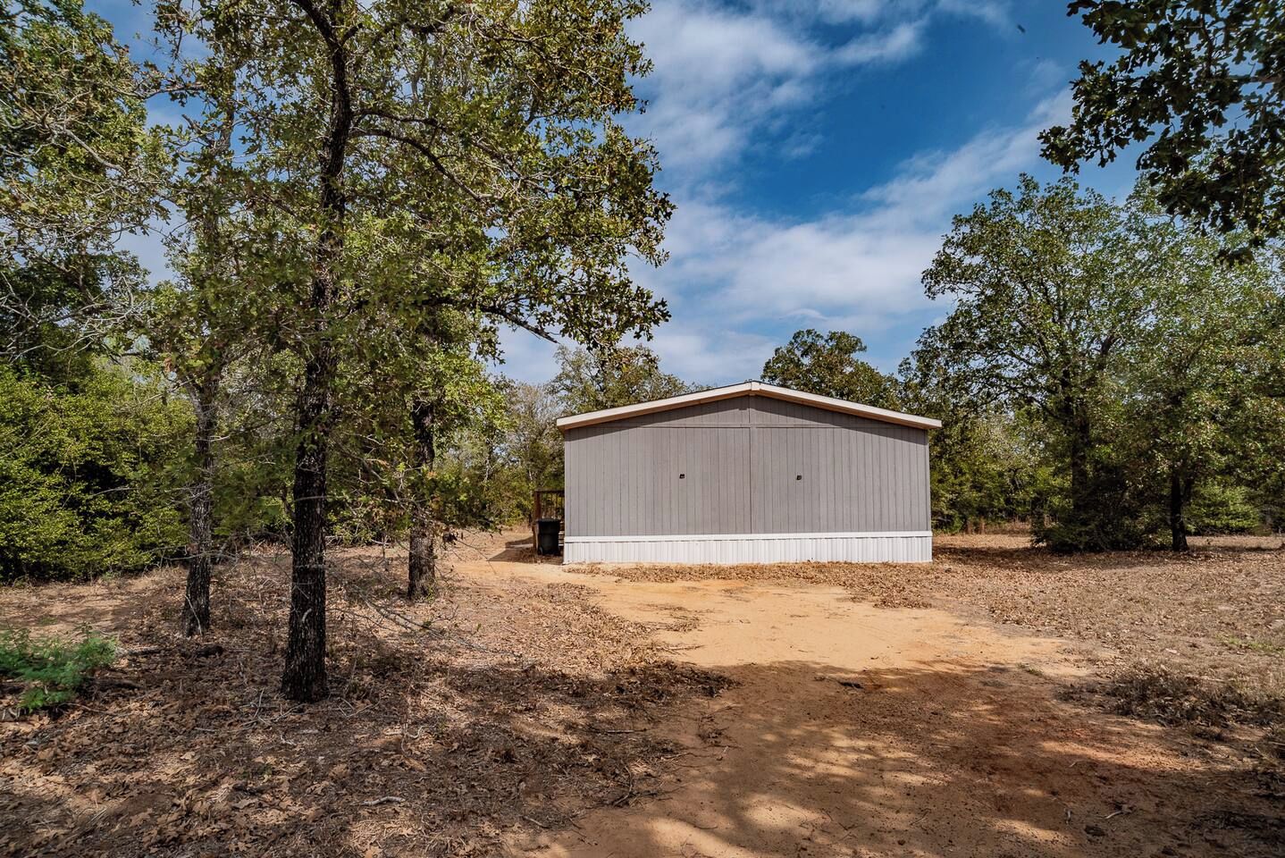 A single-story building with a flat roof, surrounded by trees and a dirt path leading to it.