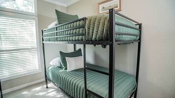 A bunk bed with green bedding and pillows, a window with blinds, and a framed picture on the wall.