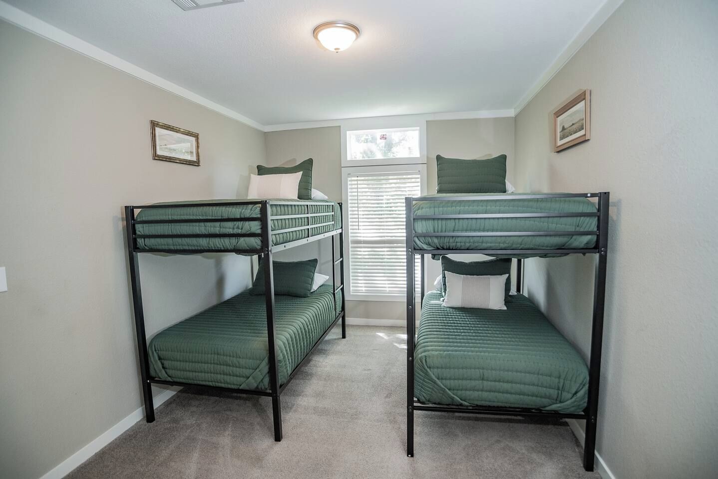 Une chambre avec deux lits superposés, une fenêtre avec des stores et un luminaire au plafond.