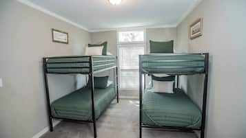 Une chambre avec deux lits superposés, une fenêtre avec des stores et un luminaire au plafond.