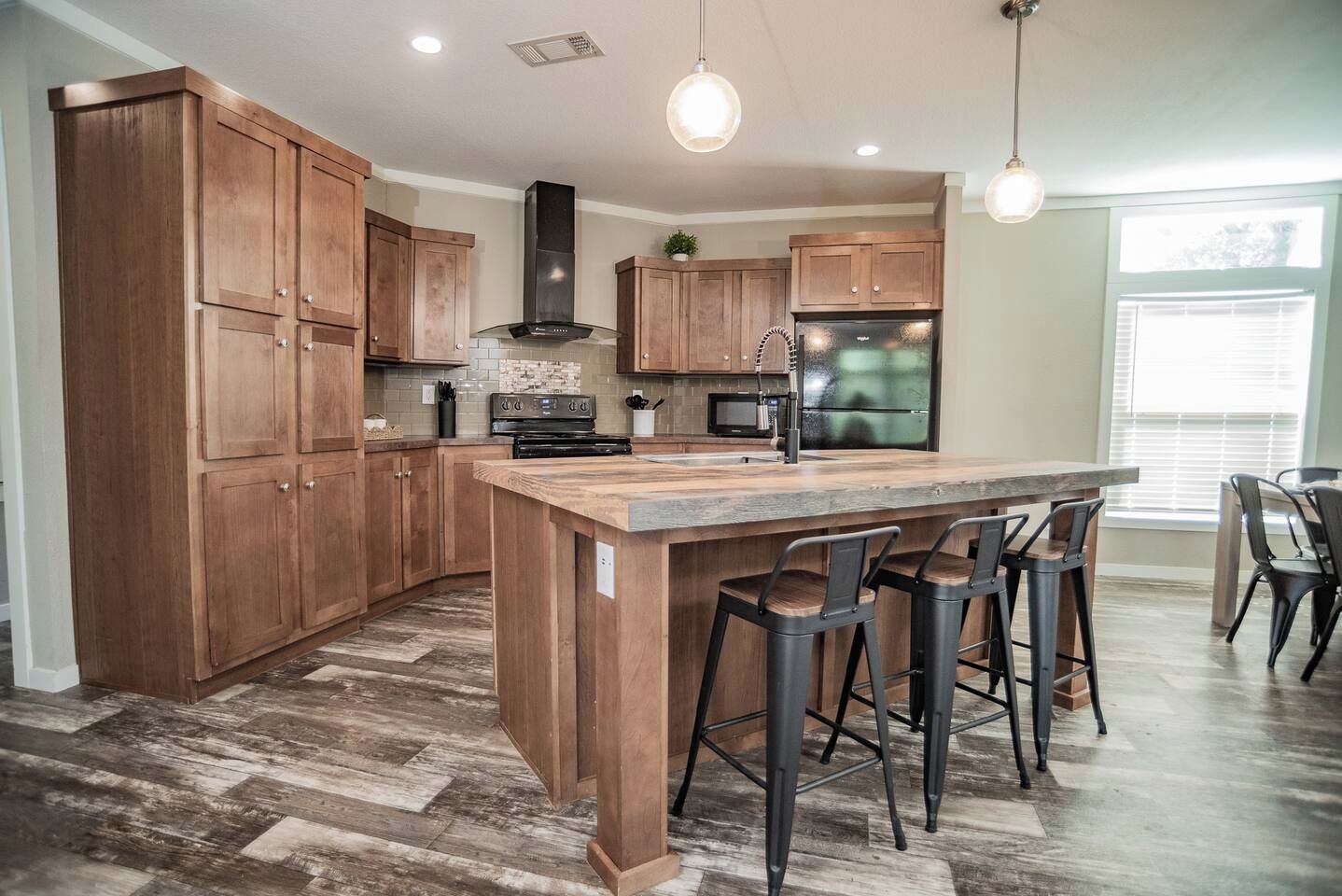 A kitchen with wooden cabinets, a central island with bar stools, a stainless steel refrigerator, and a microwave.