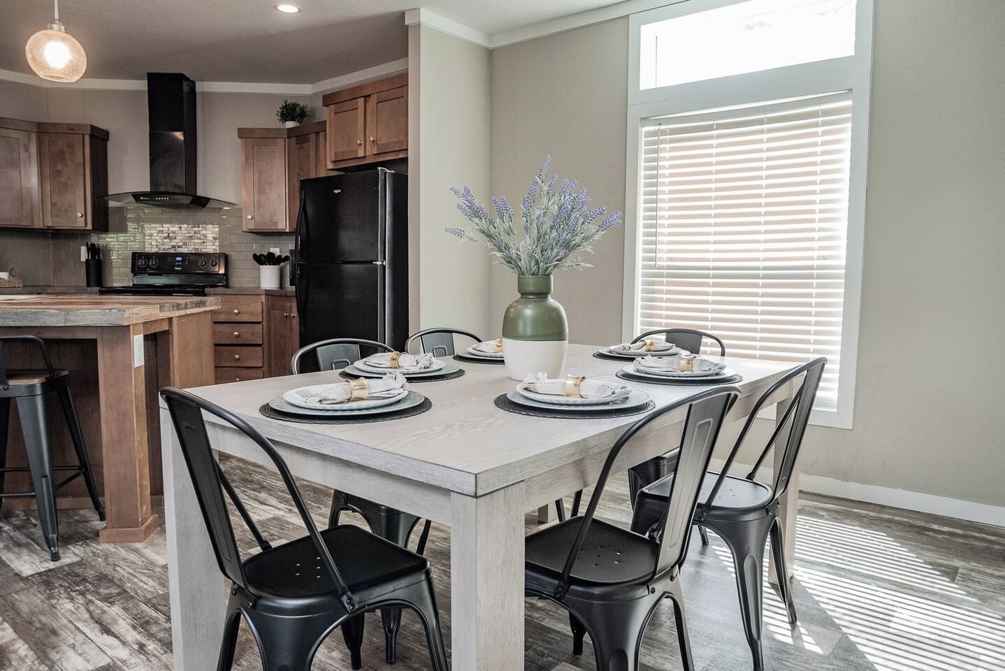 A dining area with a table set for four, surrounded by chairs, in a room with a kitchen in the background.