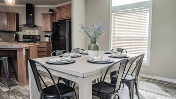 A dining area with a table set for four, surrounded by chairs, in a room with a kitchen in the background.