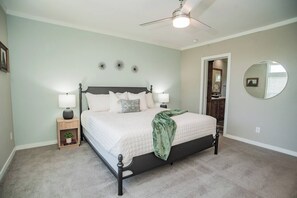 Een slaapkamer met een bed, bedlampjes, een nachtkastje, een spiegel en een plafondventilator.